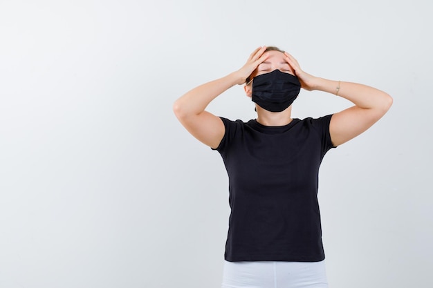 Blonde girl holding hands on forehead in black t-shirt isolated