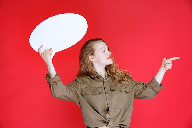 Blonde girl holding an ovale thinkboard and pointing at it.