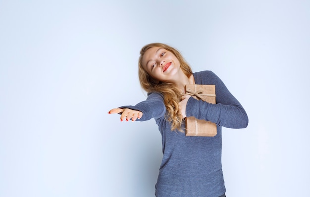 Ragazza bionda che abbraccia stretto il suo contenitore di regalo di cartone.