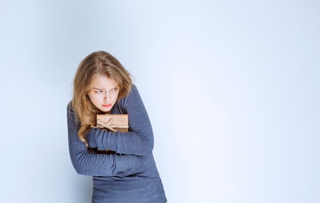 Free photo blonde girl hugging her cardboard gift box tight.