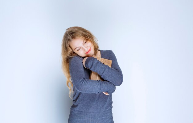 Blonde girl hugging her cardboard gift box tight. 