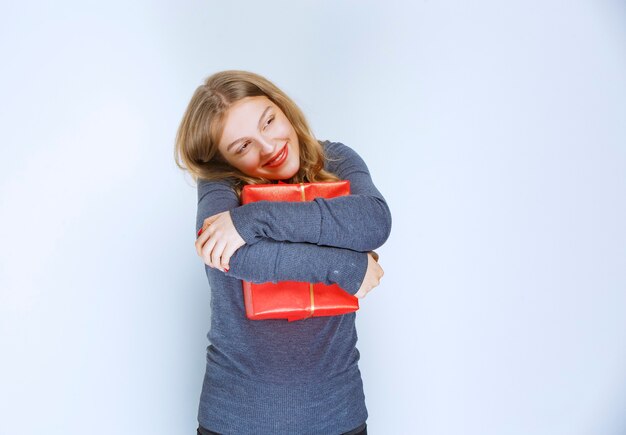 Blonde girl hugging her red gift box and feeling happy.