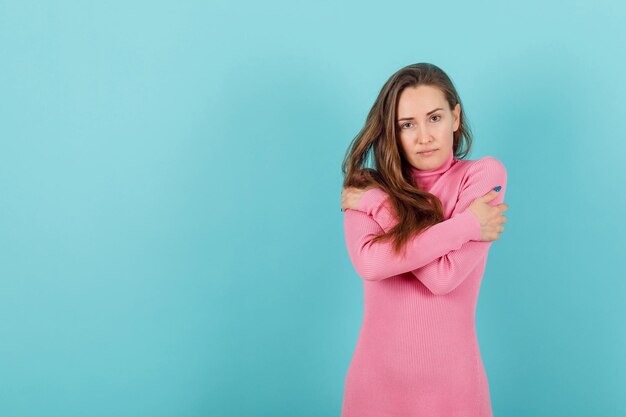 Blonde girl is crossing arms by feeling cold on blue background