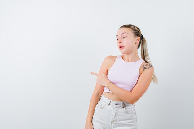 Blonde girl is pointing her left side on white background