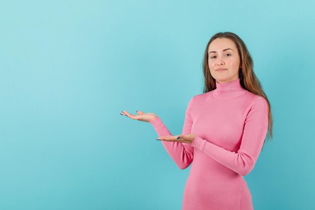 Blonde girl is pointing to left with hands on blue background