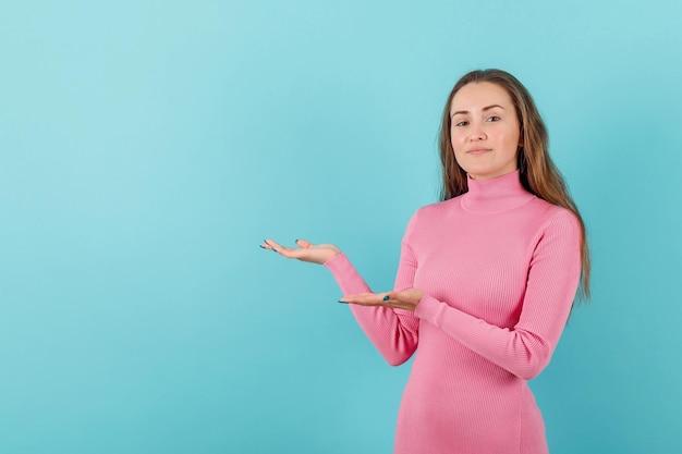 Blonde girl is pointing to left with hands on blue background