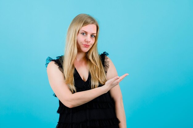 Blonde girl is pointing right with hand on blue background