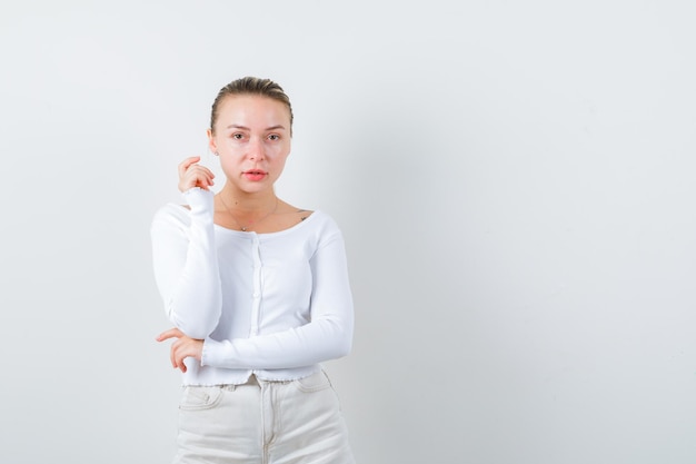 ブロンドの女の子は白い背景の上のカメラのポーズをとっています