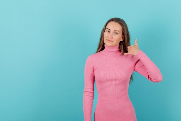 Blonde girl is showing phone gesture with hand on blue background