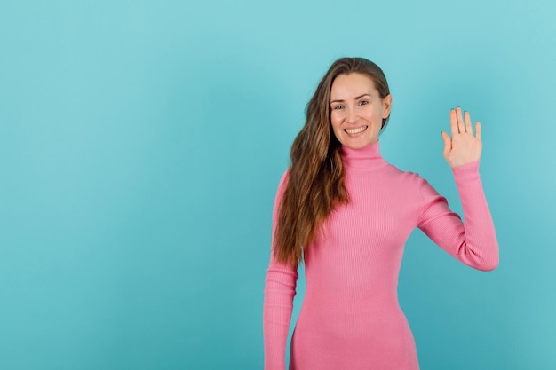 Blonde girl is smiling by raising up her hand on blue background