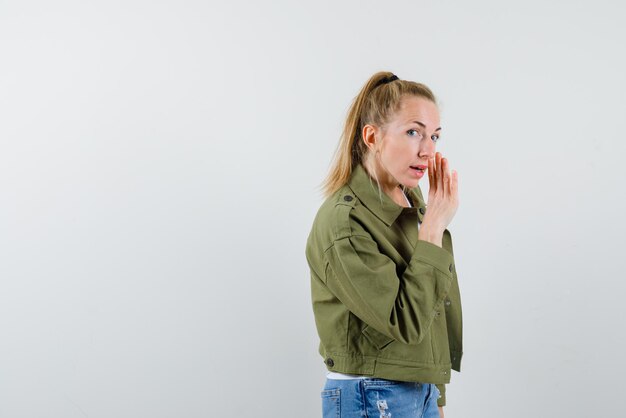 The blonde girl is touching by her right hand to mouth on white background