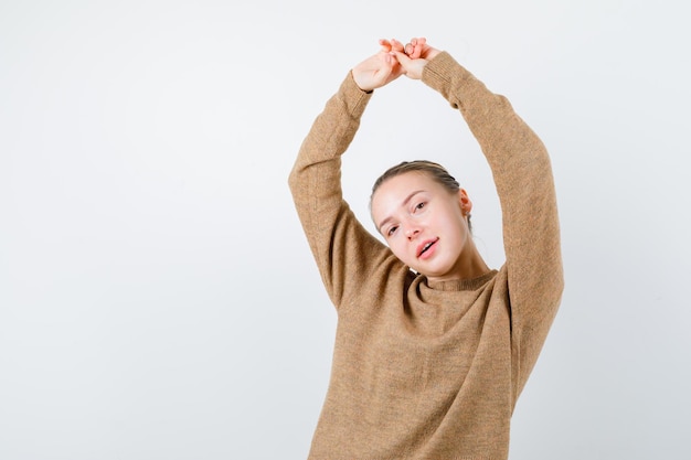 La ragazza bionda unisce le mani nella sua testa su sfondo bianco