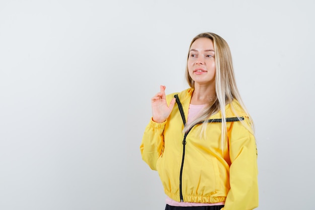 Blonde girl keeping fingers crossed in yellow jacket and looking hopeful.