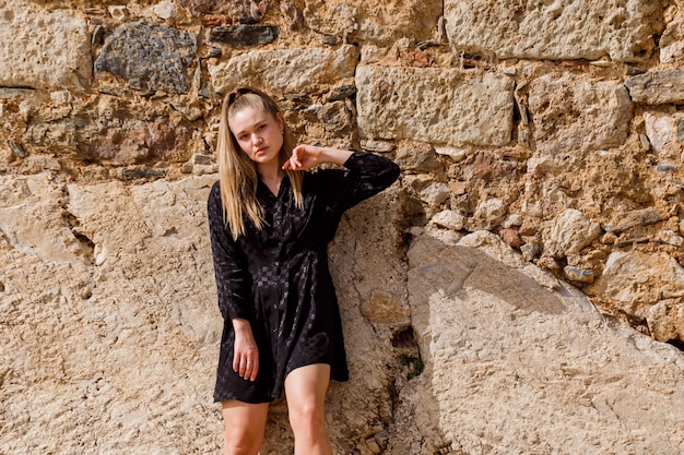 The blonde girl look at the left in black dress on stone background