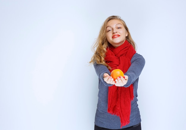 Blonde girl offering an orange fruit.