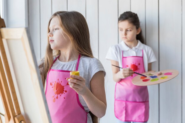 無料の写真 イーゼルと彼女の友人の背景の後ろに立っているブロンドの女の子