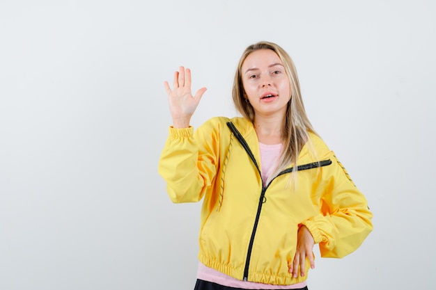 ピンクのTシャツと黄色のジャケットのブロンドの女の子が一時停止の標識を示し、真剣に見える