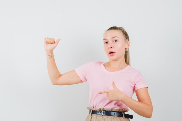 脇を向いて、Tシャツ、ズボンで腕を上げ、自信を持って見えるブロンドの女の子、正面図。