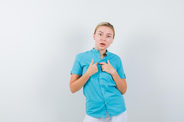 Blonde girl pointing at herself with index fingers in blue blouse isolated