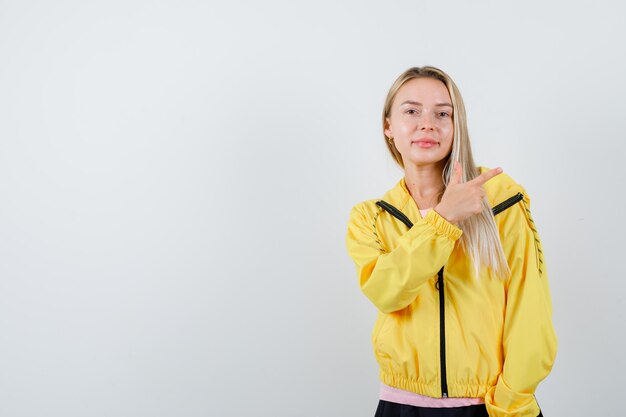 분홍색 티셔츠와 노란색 재킷에 오른쪽을 가리키고 행복을 찾는 금발 소녀.