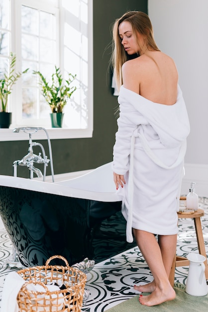 Блондинка позирует в ванной с банным халатом