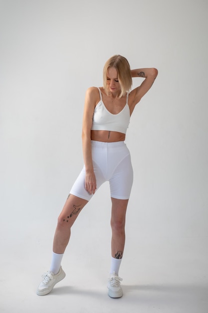 Blonde girl posing on a white background in a top and leggings