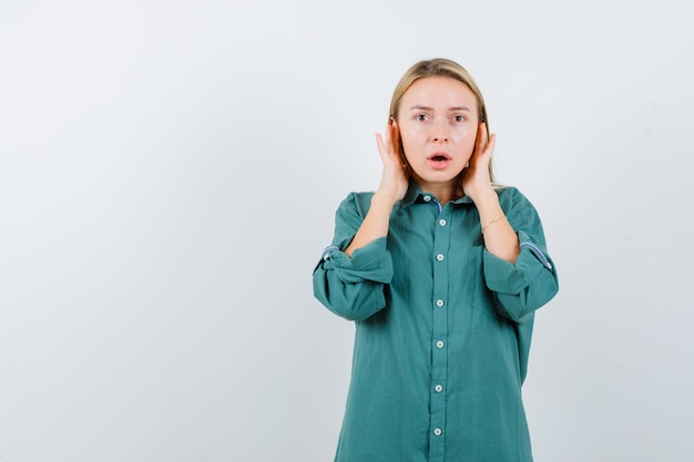 Blonde girl pressing hands on ears in green blouse and looking shocked