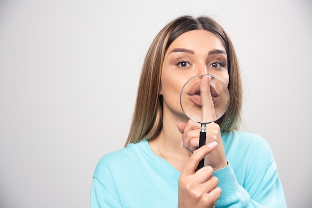 Ragazza bionda che mette una lente d'ingrandimento alla sua bocca.