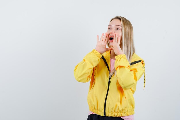 Blonde girl shouting or announcing something in yellow jacket and looking excited.