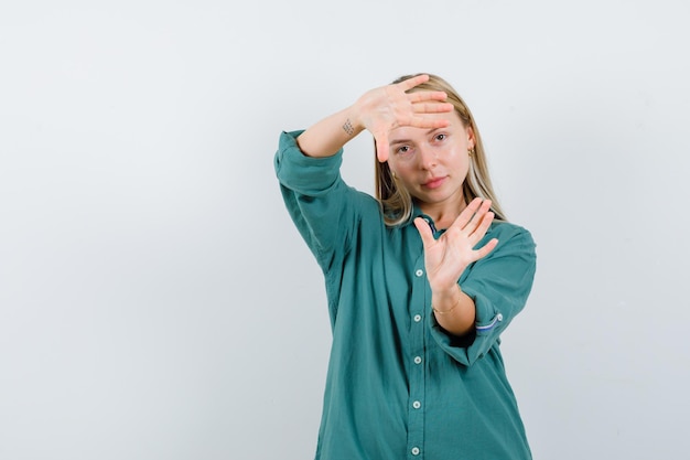 Blonde girl showing frame gesture in green blouse and looking happy.