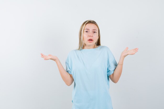 Blonde girl showing helpless gesture in blue t-shirt and looking confused. front view.