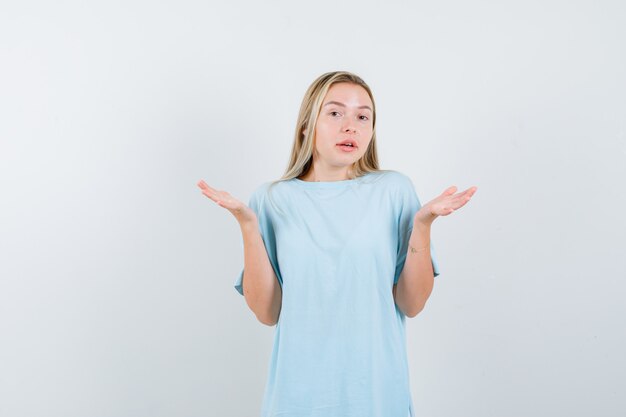 Blonde girl showing helpless gesture in blue t-shirt and looking confused. front view.