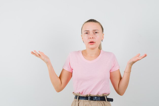 Blonde girl showing helpless gesture in t-shirt, pants and looking confused. front view.