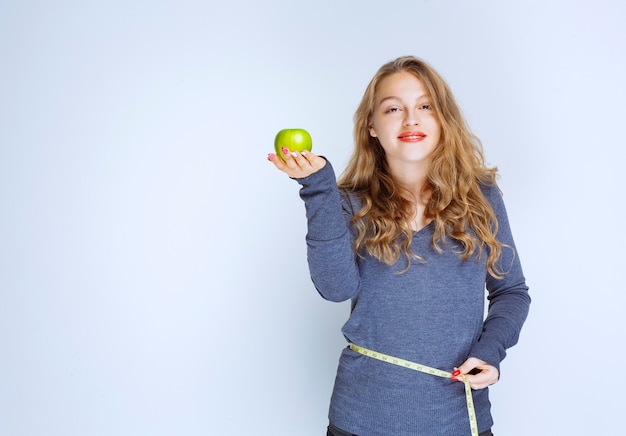 Blonde girl showing her waist size while holding a green apple.