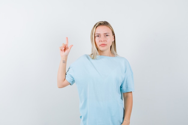 Блондинка показывает жест в синей футболке и серьезно, вид спереди.