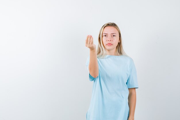 青いTシャツでイタリアのジェスチャーを示し、真剣に見えるブロンドの女の子、正面図。