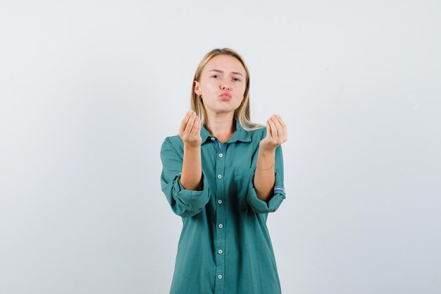 Blonde girl showing Italian gesture in green blouse and looking satisfied.