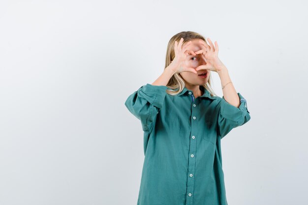 Blonde girl showing love gesture with hands in green blouse and looking enchanting