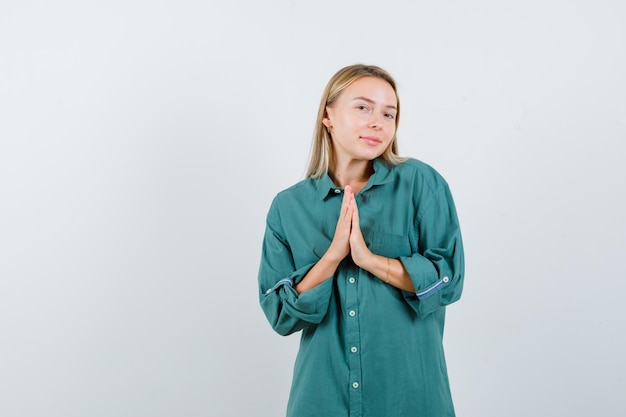 Foto gratuita ragazza bionda che mostra gesto di namaste in camicetta verde e sembra ottimista