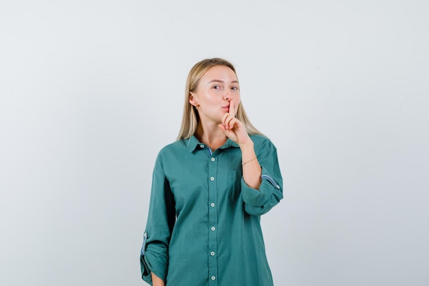 Blonde girl showing silence gesture in green blouse and looking pretty.