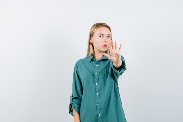 Blonde girl showing stop sign in green blouse and looking serious.