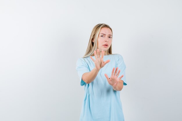 Blonde girl showing stop signs in blue t-shirt and looking uncomfortable , front view.