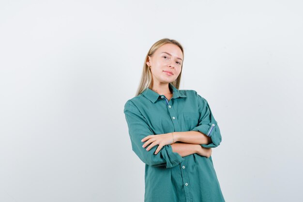 Blonde girl standing arms crossed in green blouse and looking happy.