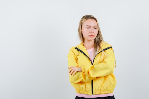 금발 소녀 서있는 팔은 분홍색 티셔츠와 노란색 재킷에 교차하고 잠겨있는 찾고.