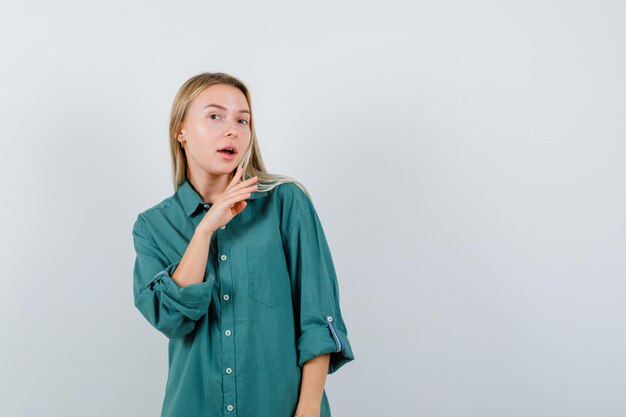 Blonde girl stretching hand near mouth in green blouse and looking pretty