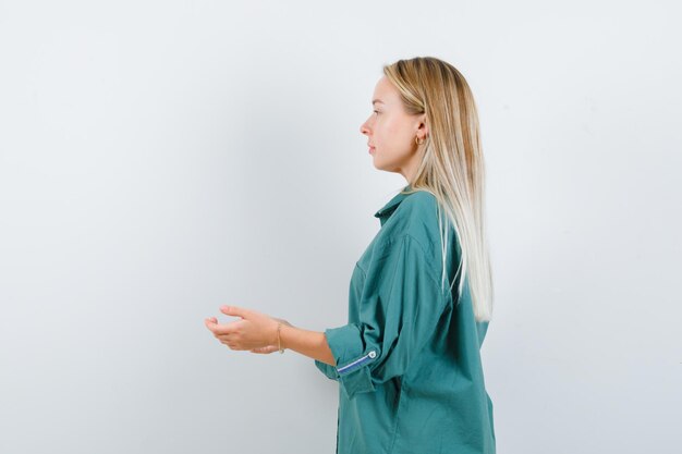 Blonde girl stretching hands as receiving something in green blouse and looking pretty.