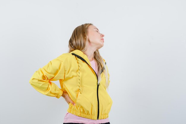 Blonde girl suffering from backache in yellow jacket and looking fatigued.