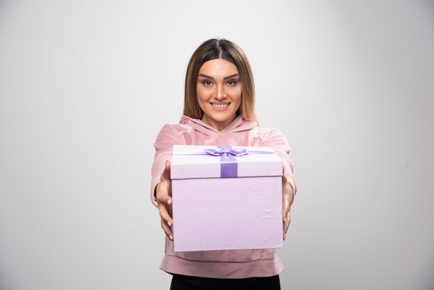 Blonde girl in sweatshirt offering a gift box