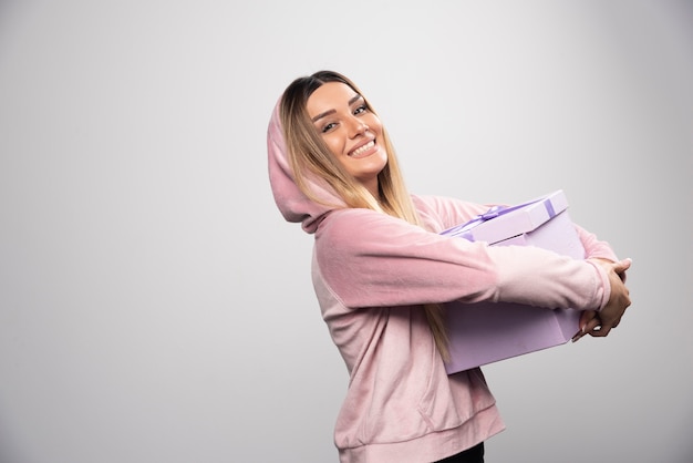 Blonde girl in sweatshirt received a gift box and feels positively surprized