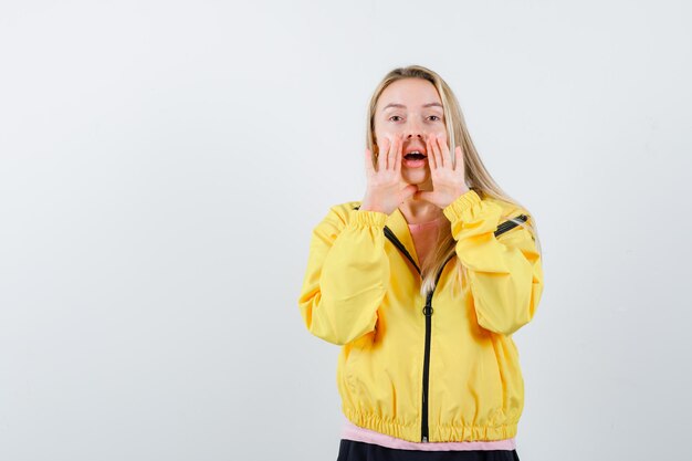 Blonde girl telling secret with hands near mouth in yellow jacket and looking cute